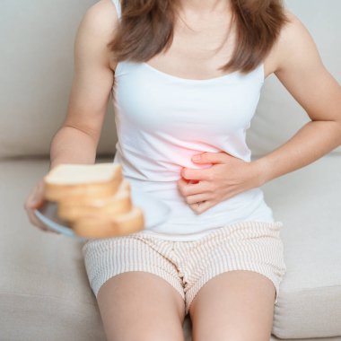 Glüten intoleransı, glütensiz ve çölyak hastalığı veya buğday alerjisi konsepti. Glüten yedikten sonra karın ağrısı çeken bir kadın. Mide ağrısı, mide bulantısı, şişkinlik, gaz, ishal ve deri döküntüsü.