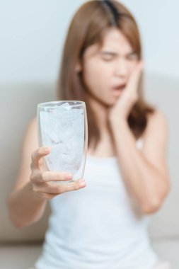 Dişler Soğuğa Duyarlı konsepti. Kadın elinde buzlu su bardağı ile yemekten sonra diş ağrısı ve ağrı çekiyor. Diş çürüğü veya Sakız Hastalığı, Öğütücü Diş ve Stres, Korunmasız Sinir Kökleri, Çatlak ve Alınan Dişetleri