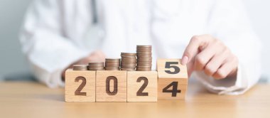 2024 yılı sonunda Doktor ve madeni paralarla mutlu yıllar 2025 'e. Para yığını depozito, sağlık giderleri, para tasarrufu, sağlık sigortası, sağlık, bağış ve finans konsepti