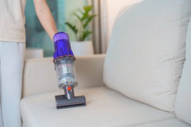 Kablosuz elektrik süpürgesiyle kanepeyi temizleyen kadın. Ev hanımı kablosuz süpürgeyi evi temizlemek için kullanıyor. Ev işleri, Temizlik, Temizlik, Temizlik, Toz, Temizlik ve günlük rutin