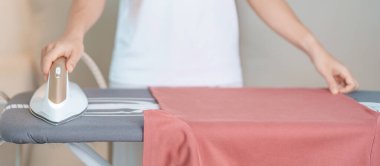 Kadın ütü masasında elektrikli ütü ütülü tişört, akıllı otomatik buhar ütüsü tutuyor. Çamaşır, ev işleri, temizlik, ev temizliği, ev işleri ve günlük rutin konsept.