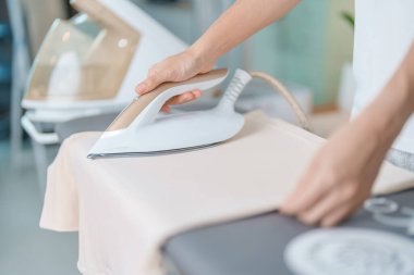 Kadın ütü masasında elektrikli ütü ütülü tişört, akıllı otomatik buhar ütüsü tutuyor. Çamaşır, ev işleri, temizlik, ev temizliği, ev işleri ve günlük rutin konsept.