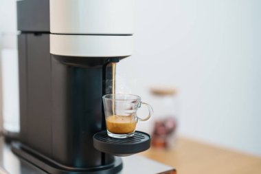 Kahve yaparken buharlı ve köpüklü Espresso bardağı. Kahve makinesinin yaptığı kahve, ahşap masa tezgahında. Kafe, günlük içecek içeceği Ev, Daire ve Ofis konsepti