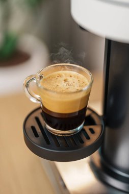 Kahve yaparken buharlı ve köpüklü Espresso bardağı. Kahve makinesinin yaptığı kahve, ahşap masa tezgahında. Kafe, günlük içecek içeceği Ev, Daire ve Ofis konsepti