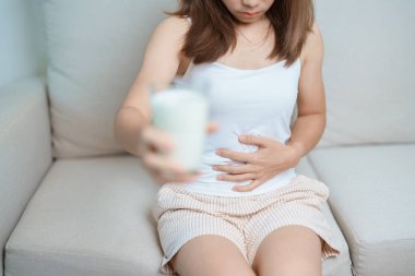 Laktoz intoleransı ve süt alerjisi konsepti. Kadın süt bardağı tutuyor ve karın krampları ve inek sütü içerken ağrı yapıyor. Semptom mide ağrısı, süt ürünlerine duyarlılık, mide bulantısı, şişkinlik, gaz ve ishal.