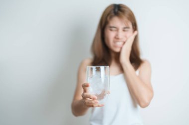 Dişler Soğuğa Duyarlı konsepti. Kadın elinde buzlu su bardağı ile yemekten sonra diş ağrısı ve ağrı çekiyor. Diş çürüğü veya Sakız Hastalığı, Öğütücü Diş ve Stres, Korunmasız Sinir Kökleri, Çatlak ve Alınan Dişetleri