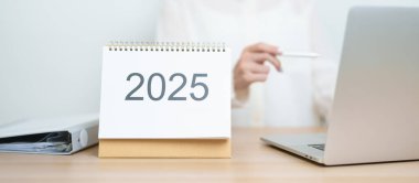 2025 Yıllık Takvim, iş kadınlarıyla masada dizüstü bilgisayar kullanarak, çalışarak ve yazarak. Geri sayım, Mutlu Yıllar, Çözünürlük, Yıl sonu ve Yeni Başlangıç ve Hedefler Planlama Eylemi