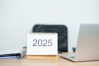 2025 Yıllık Takvim, ofiste çalışırken ve yazarken dizüstü bilgisayarla masada. Geri sayım, Mutlu Yıllar, Çözünürlük, Yıl sonu ve Yeni Başlangıç ve Hedefler Planlama Eylemi
