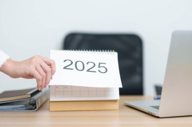 İş kadını, ofiste çalışırken ve yazarken 2025 Yıllık Takvimi dizüstü bilgisayarla değiştiriyor. Geri sayım, Mutlu Yıllar, Çözünürlük, Yıl sonu ve Yeni Başlangıç ve Hedefler Planlama Eylemi