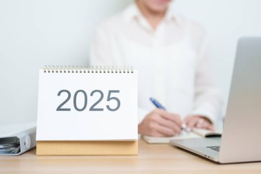 2025 Yıllık Takvim, iş kadınlarıyla masada dizüstü bilgisayar kullanarak, çalışarak ve yazarak. Geri sayım, Mutlu Yıllar, Çözünürlük, Yıl sonu ve Yeni Başlangıç ve Hedefler Planlama Eylemi