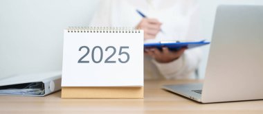 2025 Yıllık Takvim, iş kadınlarıyla masada dizüstü bilgisayar kullanarak, çalışarak ve yazarak. Geri sayım, Mutlu Yıllar, Çözünürlük, Yıl sonu ve Yeni Başlangıç ve Hedefler Planlama Eylemi