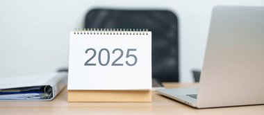 2025 Yıllık Takvim, ofiste çalışırken ve yazarken dizüstü bilgisayarla masada. Geri sayım, Mutlu Yıllar, Çözünürlük, Yıl sonu ve Yeni Başlangıç ve Hedefler Planlama Eylemi