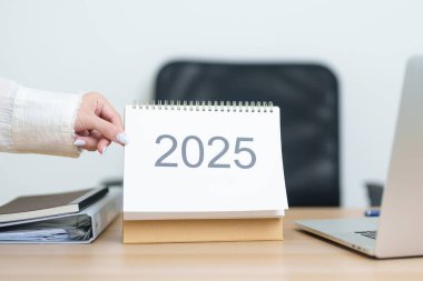 İş kadını, ofiste çalışırken ve yazarken 2025 Yıllık Takvimi dizüstü bilgisayarla değiştiriyor. Geri sayım, Mutlu Yıllar, Çözünürlük, Yıl sonu ve Yeni Başlangıç ve Hedefler Planlama Eylemi