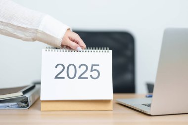 İş kadını, ofiste çalışırken ve yazarken 2025 Yıllık Takvimi dizüstü bilgisayarla değiştiriyor. Geri sayım, Mutlu Yıllar, Çözünürlük, Yıl sonu ve Yeni Başlangıç ve Hedefler Planlama Eylemi