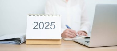 2025 Yıllık Takvim, iş kadınlarıyla masada dizüstü bilgisayar kullanarak, çalışarak ve yazarak. Geri sayım, Mutlu Yıllar, Çözünürlük, Yıl sonu ve Yeni Başlangıç ve Hedefler Planlama Eylemi