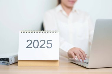 2025 Yıllık Takvim, iş kadınlarıyla masada dizüstü bilgisayar kullanarak, çalışarak ve yazarak. Geri sayım, Mutlu Yıllar, Çözünürlük, Yıl sonu ve Yeni Başlangıç ve Hedefler Planlama Eylemi