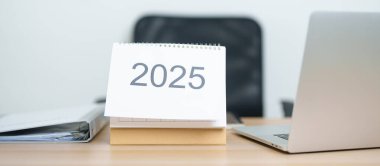 2025 Yıllık Takvim, ofiste çalışırken ve yazarken dizüstü bilgisayarla masada. Geri sayım, Mutlu Yıllar, Çözünürlük, Yıl sonu ve Yeni Başlangıç ve Hedefler Planlama Eylemi