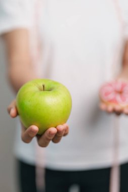 Kadın elini yeşil elma ve çörek ile tutar, kadın fitness meyve ve tatlı sağlıklı ve sağlıksız abur cubur arasında seçim yapar. Diyet kontrolü, kilo kaybı, obezite, yeme tarzı ve beslenme konsepti