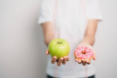 Kadın elini yeşil elma ve çörek ile tutar, kadın fitness meyve ve tatlı sağlıklı ve sağlıksız abur cubur arasında seçim yapar. Diyet kontrolü, kilo kaybı, obezite, yeme tarzı ve beslenme konsepti