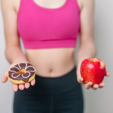 woman hand hold red Apple and donut, female fitness choose between fruit is Healthy and sweet is Unhealthy junk food. Dieting control, Weight loss, Obesity, eating lifestyle and nutrition concept clipart