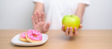 Kadın ellerinin yeşil elma tutması ve çöreği reddetmesi, kadın fitness seçimiyle meyve sağlıklı ve tatlı, sağlıksız abur cuburdur. Diyet kontrolü, kilo kaybı, obezite, yeme tarzı ve beslenme