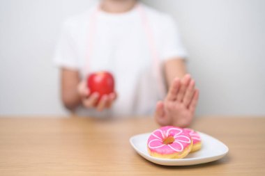 Kadın eli kırmızı elma tutuyor ve donutu reddediyor, kadın spor salonu meyvelerle sağlıklı ve tatlı sağlıklı olmayan abur cuburlar arasında seçim yapıyor. Diyet kontrolü, kilo kaybı, obezite, yeme tarzı ve beslenme