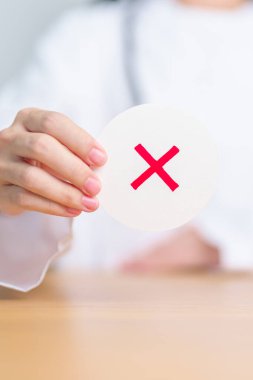 Doktor yanlış sembol kağıdı gösterdi. Doğru ve yanlış, kabul et ve reddet, değerlendirme, tanı, oy ver, anket, evet veya hayır, sağlık, tıbbi ve araştırma kavramları