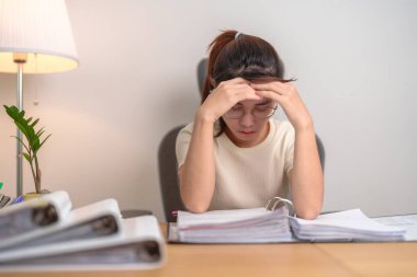 Çalışırken yorgun ve stresli olan Asyalı bir kadın, baş ağrısı çeken bir iş kadını, ofisinde migren ağrısı olan bir kadın, gece geç saatlerde evinde dosya yığını olan bitkin bir kadın. Fazla çalışma ve fazla mesai