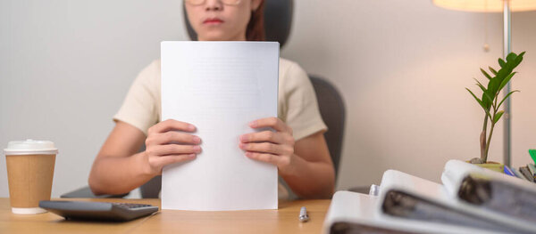 Азиатка усердно работает с папкой финансовых отчетов, женщина-предприниматель подписывает контракт или читает документы бумаги дома или в офисе поздно вечером. Переработанная, упорно работающая и бизнес-концепция