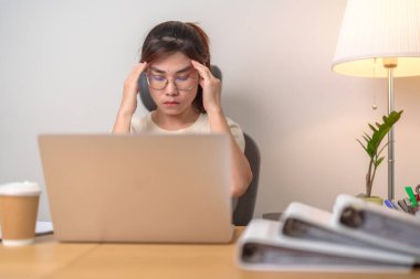 Çalışırken stresli ve yorgun Asyalı kadın, baş ağrısı çeken kadın iş kadını, ofiste migren ve uykulu kadın, evde bilgisayarlı yorgun kadın. Aşırı yükleme ve aşırı çalışma