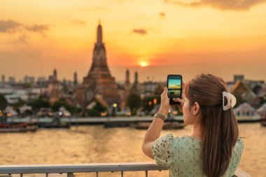 Turist kadın gün batımında Wat Arun Tapınağı 'nı seyretmeyi sever gezgin çatı katındaki bardan Temple of Dawn' a fotoğraf çeker. Bangkok, Tayland ve Güneydoğu Asya 'daki Landmark and Travel durağı