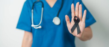 Melanoma ve cilt kanseri, aşı hasarı farkındalığı ayı ve huzur içinde yatma kavramları. Doktor elinde siyah kurdele tutuyor.