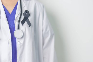 Melanoma ve cilt kanseri, aşı hasarı farkındalığı ayı ve huzur içinde yatma kavramları. Doktor elinde siyah kurdele tutuyor.