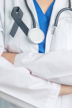 Melanoma ve cilt kanseri, aşı hasarı farkındalığı ayı ve huzur içinde yatma kavramları. Doktor elinde siyah kurdele tutuyor.