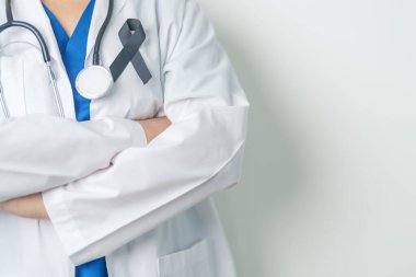 Melanoma ve cilt kanseri, aşı hasarı farkındalığı ayı ve huzur içinde yatma kavramları. Doktor elinde siyah kurdele tutuyor.