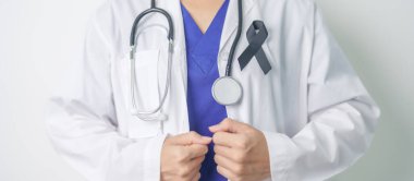 Melanoma ve cilt kanseri, aşı hasarı farkındalığı ayı ve huzur içinde yatma kavramları. Doktor elinde siyah kurdele tutuyor.