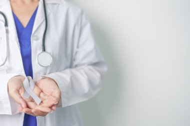 Beyin Kanseri Farkındalığı Mayıs ayında, gri renkli kurdeleli doktor, yaşam insanlarını desteklediği için. Sağlık ve Dünya Kanser Günü konsepti