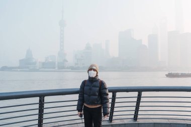 young Asian woman wearing respiratory mask protect and filter pm or particulate matter against bad Air Pollution in Shanghai City, China. Air Quality Index, AQI, Unhealthy, healthcare concept clipart