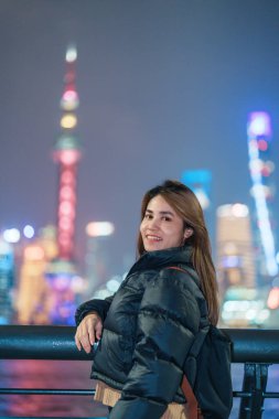 woman traveler visiting in Shanghai, China. Happy Female Tourist sightseeing Shanghai view of Lujiazui in The Bund of Shanghai at night. landmark and popular for tourism attractions. Vacation concept clipart