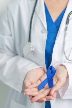 March Colectal Kanser Farkındalığı Ayı. Koyu mavi kurdeleli bir doktor. Yaşayan ve hastalıklı insanları destekliyor. Sağlık, umut ve Dünya Kanser Günü konsepti