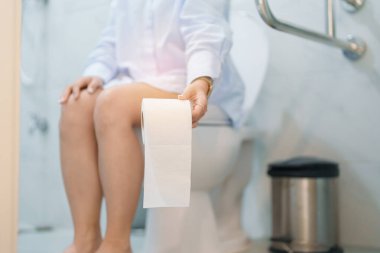 Tuvalet deliğinde otururken elinde tuvalet kağıdı tutan kadın. Sindirim, kabızlık, gıda zehirlenmesi, enfeksiyon, abdominal, mide ağrısı, sistit, sigorta, sağlık ve tıbbi yardım