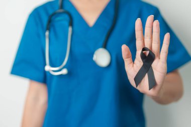 Melanoma ve cilt kanseri, aşı hasarı farkındalığı ayı ve huzur içinde yatma kavramları. Doktor elinde siyah kurdele tutuyor.