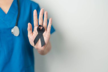 Melanoma ve cilt kanseri, aşı hasarı farkındalığı ayı ve huzur içinde yatma kavramları. Doktor elinde siyah kurdele tutuyor.