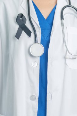 Melanoma ve cilt kanseri, aşı hasarı farkındalığı ayı ve huzur içinde yatma kavramları. Doktor elinde siyah kurdele tutuyor.