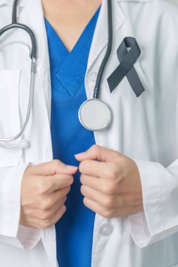 Melanoma ve cilt kanseri, aşı hasarı farkındalığı ayı ve huzur içinde yatma kavramları. Doktor elinde siyah kurdele tutuyor.