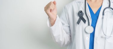 Melanoma ve cilt kanseri, aşı hasarı farkındalığı ayı ve huzur içinde yatma kavramları. Doktor elinde siyah kurdele tutuyor.