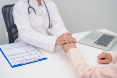 Doktor yaşlı kadın hastayla el ele tutuşuyor. Tıbbi konsültasyon sırasında empati ve destek gösteriyor. Güven, yaşlılar ve yaşlılar için sağlık, akıl sağlığı, danışmanlık ve duygusal danışmanlık 