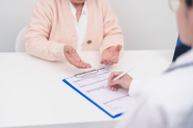 Hastanedeki doktora danışmanlık yapan kıdemli bir kadın. Yaşlı hasta konuşuyor ve hastalıkları paylaşıyor. Doktor dinler, soru sorar ve not alır. Tıbbi danışmanlık ve yaşlılık sağlığı konsepti 