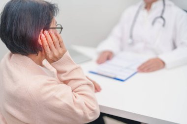 Kulak ağrısı olan yaşlı kadın hasta ve kulak hastalıkları için doktora danışmak. Kıdemli Sağlık Teşhisi. Atresia, Otitis Media, Pertorated Eardrum, Meniere Sendromu, otolaryngologist, İşitme Kaybı
