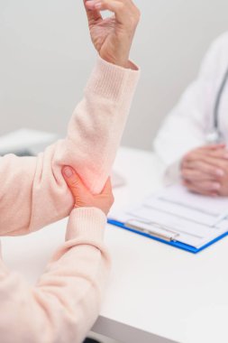 Dirsek ağrısı çeken ve hastanede danışmanlık yapan yaşlı bir kadın. Yan epikondil iltihabı ya da tenis dirseği yüzünden kas ağrısı. yaralanma, sağlık ve tıbbi danışma kavramı